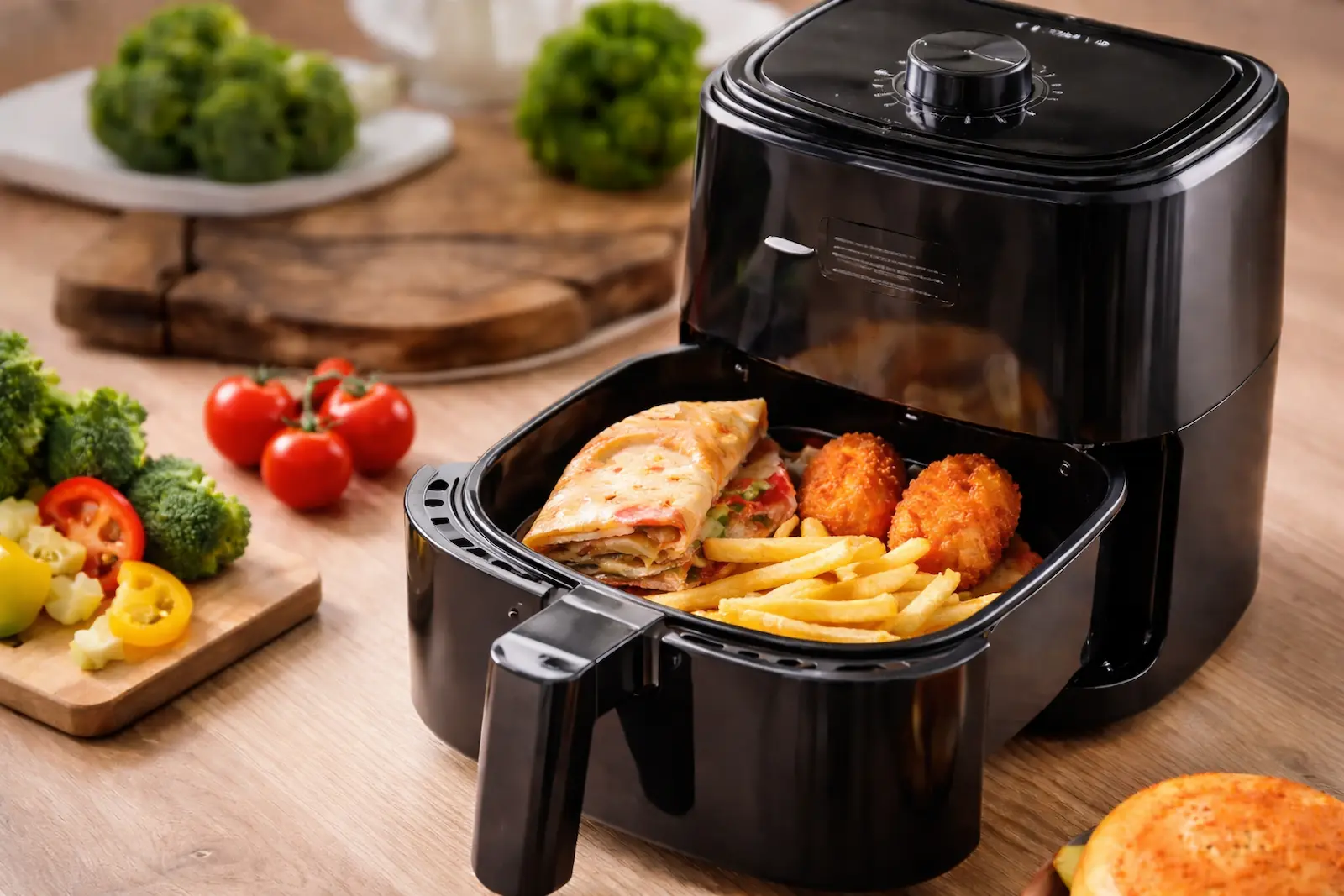 Mini-Airfryer mit kleiner Portion Pommes, panierten Snacks und Wrap im Korb auf einer Küchenarbeitsfläche